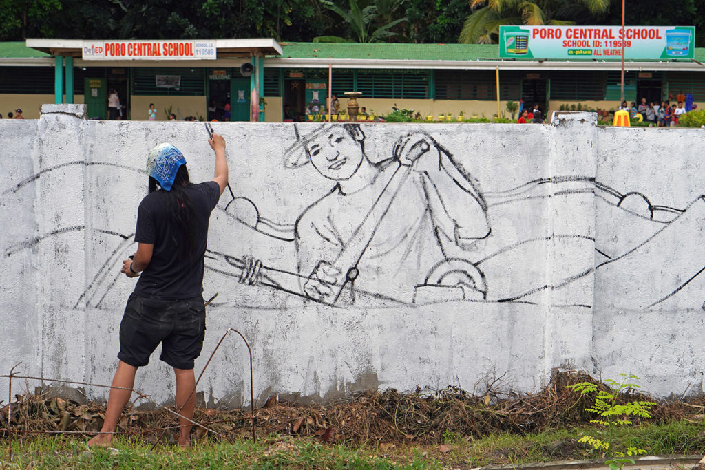 Artist AG Sano painting a mural at a school.