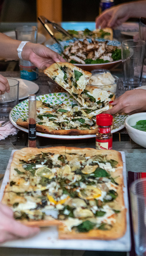 Hands reaching for slices of white pizza.