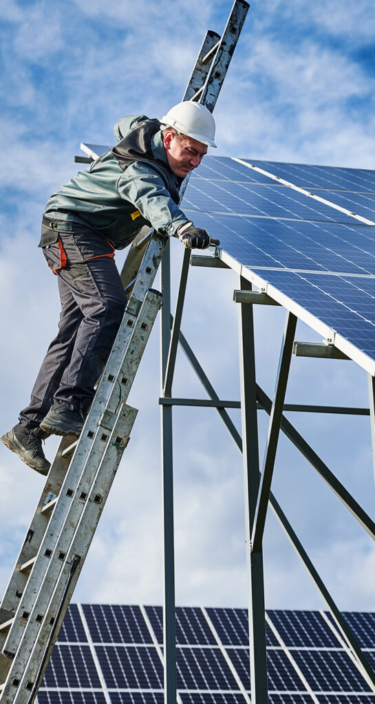 Man on a ladder servicing a solar panel.