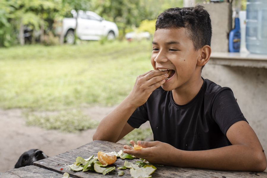 Photo of a young boy eating an orange at an outdoor table in Colombia.