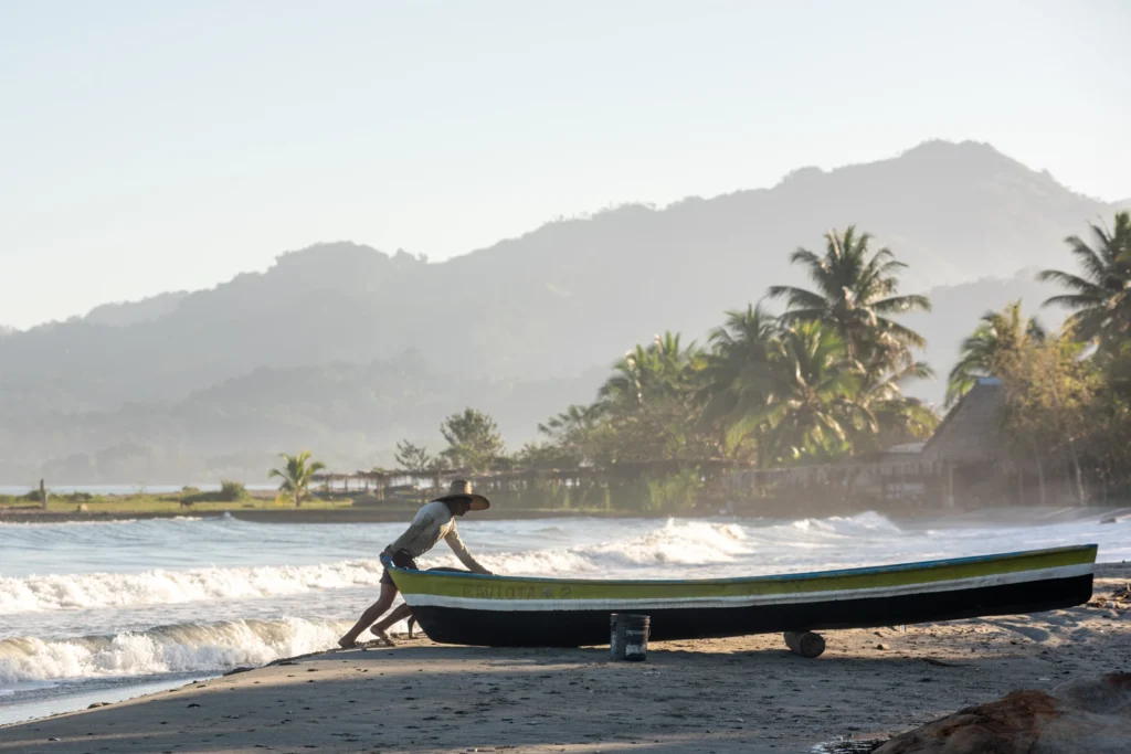 a man leans against a boat on the coastline