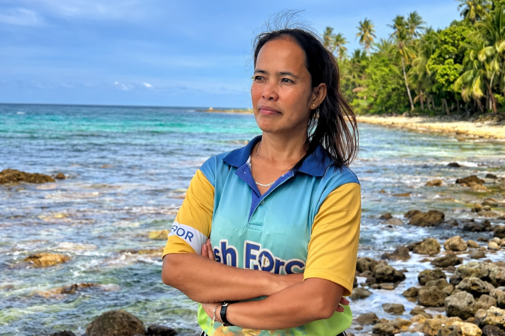 a woman standing with arms crossed and the coastline in the background
