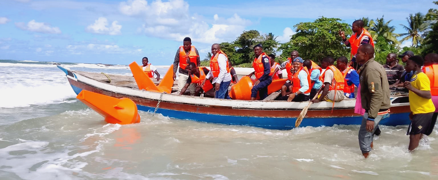 officials and community members wearing orange life jackets launching a boat off the shore with their orange buoys 