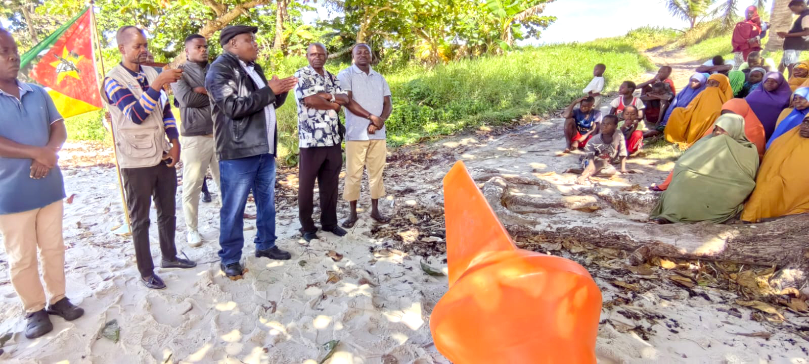 officials and community members gathered around an orange buoy on shore before it's launched into the water