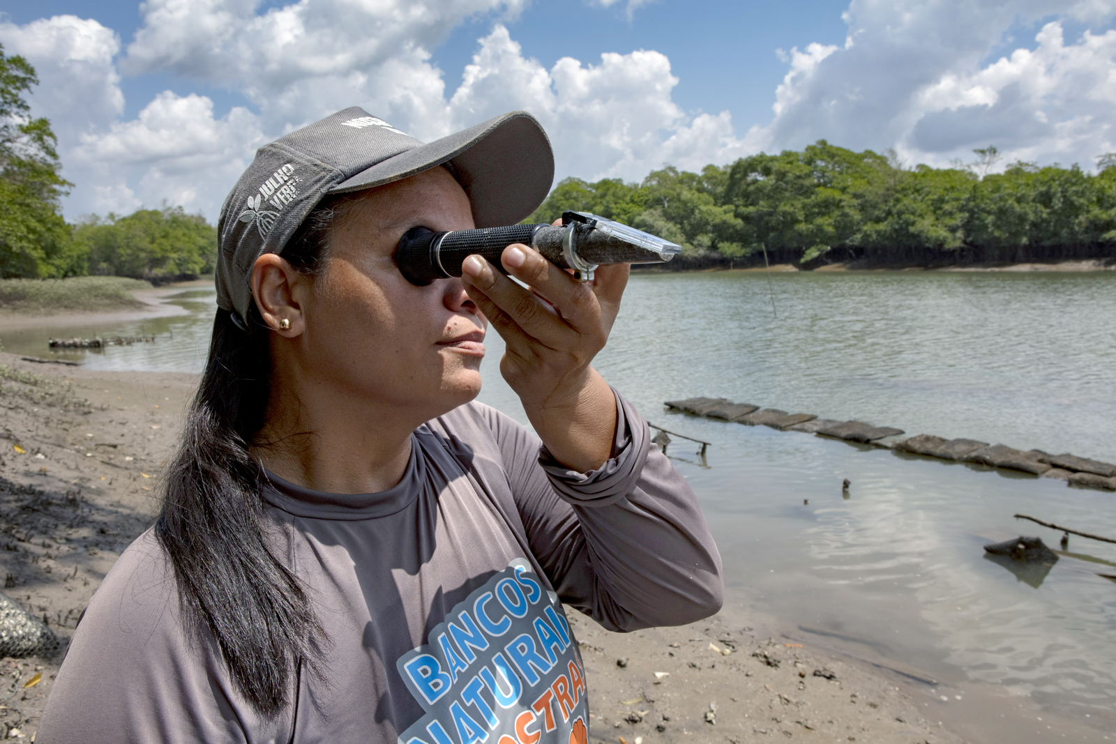 A woman holding a refractometer small device up to her eye to measure the water's salinity